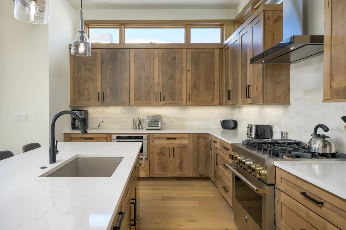 A warm and inviting kitchen featuring a large island with seating, stainless steel appliances, and natural light streaming through large windows. Wooden cabinetry adds a sense of comfort, and the overall layout encourages both cooking and social interaction.