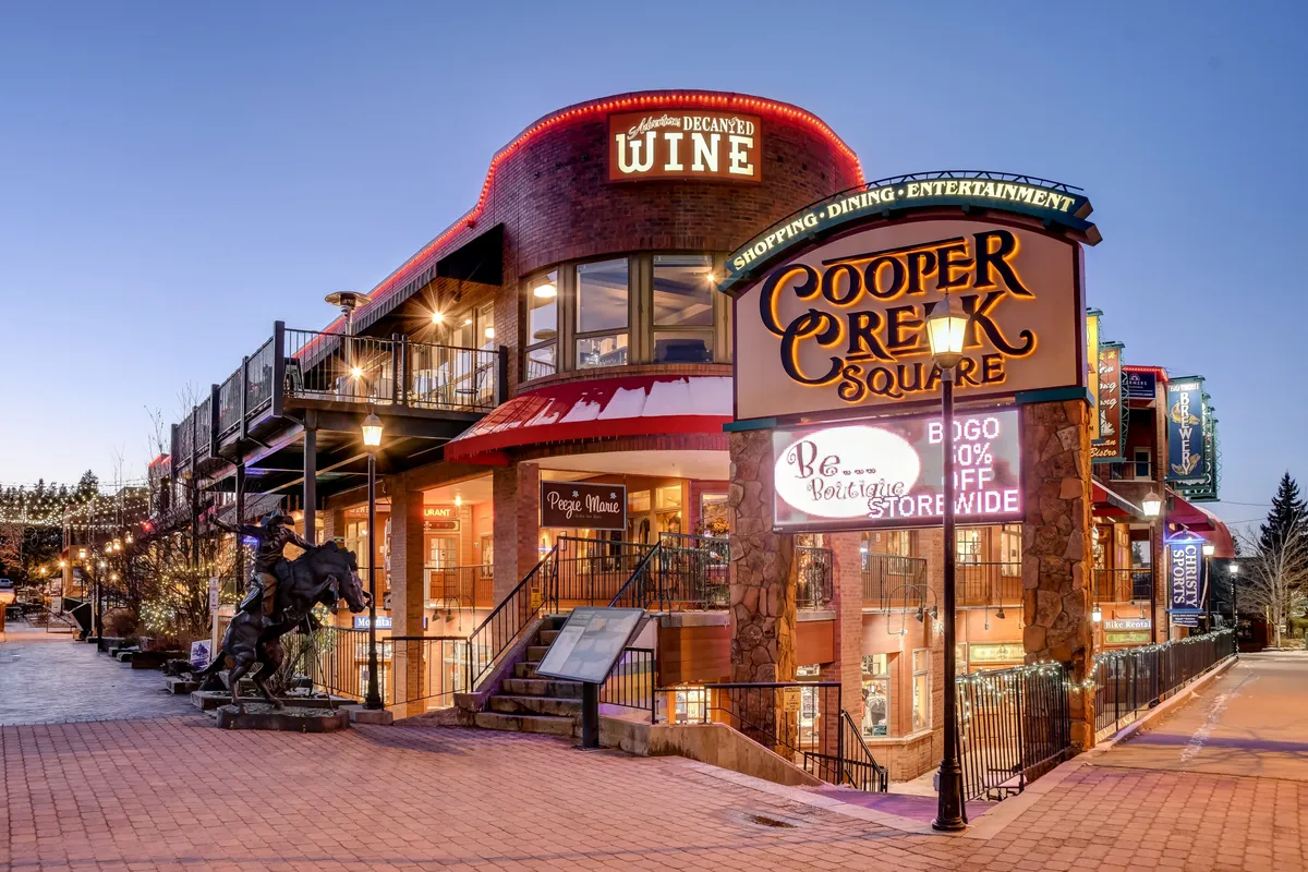 An illuminated Cooper Creek Square with decorative lighting, a prominent wine sign, and people enjoying the lively atmosphere. The scene suggests vibrant dining, shopping, and nightlife just minutes from the villa.
