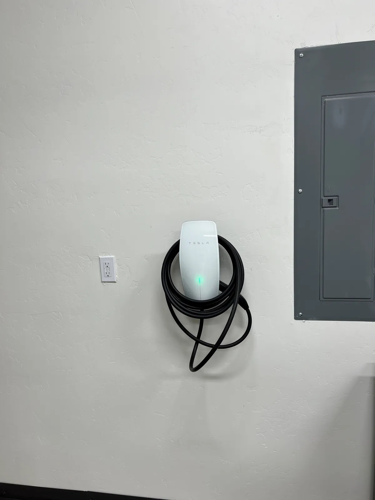A modern Tesla charging station mounted inside the villa, signaling the convenience of at-home EV charging. The setup is sleek and technologically advanced, reflecting eco-conscious living.
