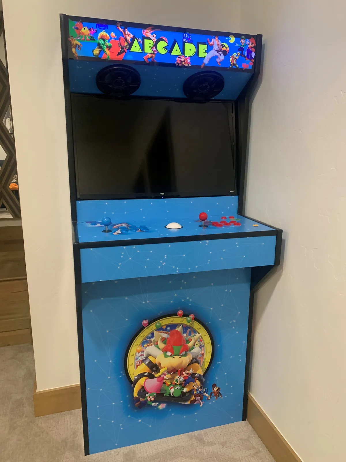 A vibrant interior den scene featuring an arcade cabinet, complete with screen and joysticks. The playful setup hints at family entertainment and leisure, echoing the inviting mood of the den space.