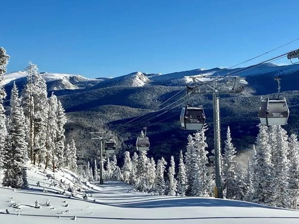 A picturesque winter scene featuring ski lift gondolas gliding above snow-covered trees, with a dramatic mountain range in the background. The bright snow and crisp light capture the energy of winter sports and mountain exploration.