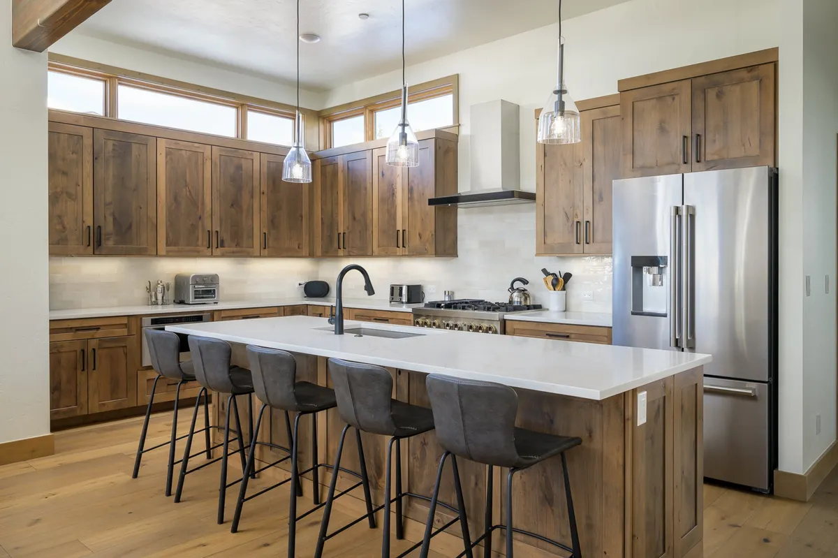A functional and modern kitchen centered around a well-appointed island with barstool seating. Stainless steel appliances and warm wood tones create a welcoming space ideal for both cooking and conversation. Pendant lighting above the island adds a touch of elegance.