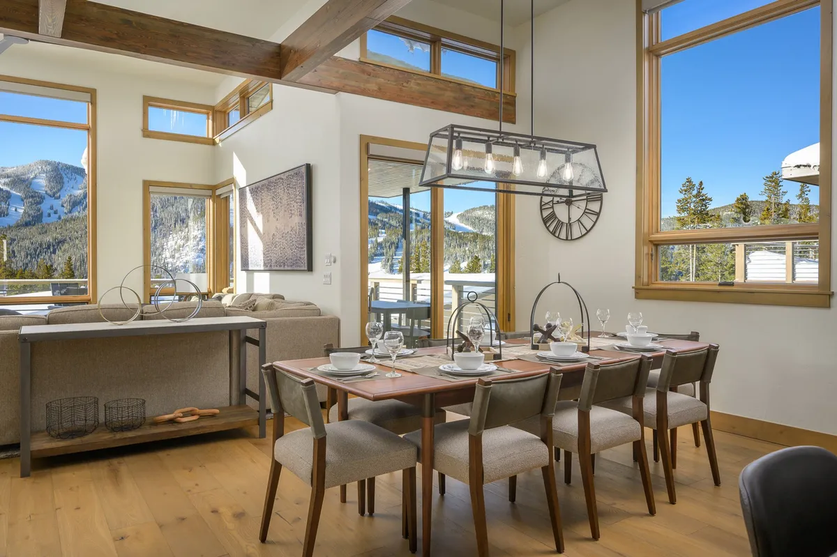 An adjacent dining area set for a meal, with large windows offering mountain views and wooden beams overhead. The setting is both cozy and refined, designed to accommodate group dining and foster memorable celebrations.