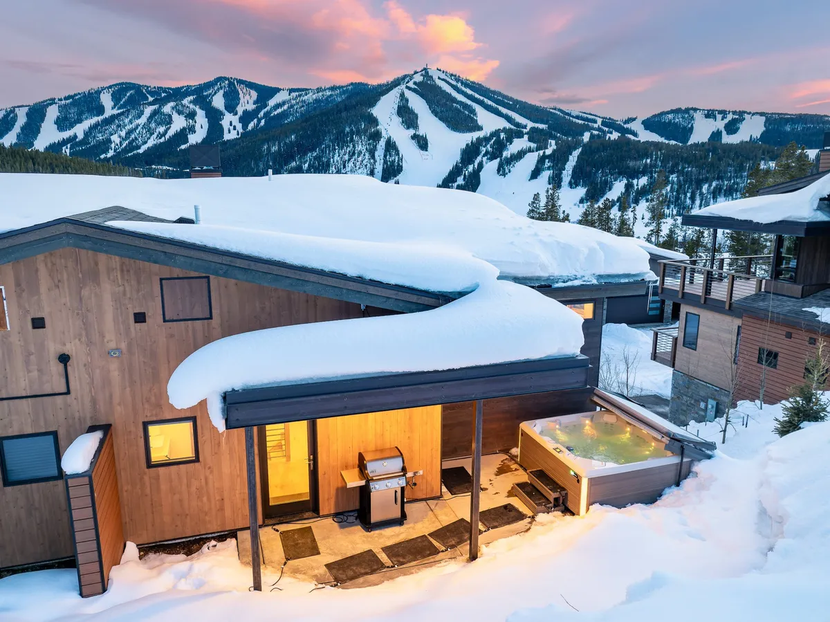 A tranquil winter scene with a private hot tub beside a snow-covered roof and a Weber grill, all set against a dramatic mountain backdrop. The deck area invites both relaxation in the hot tub and outdoor barbecuing.