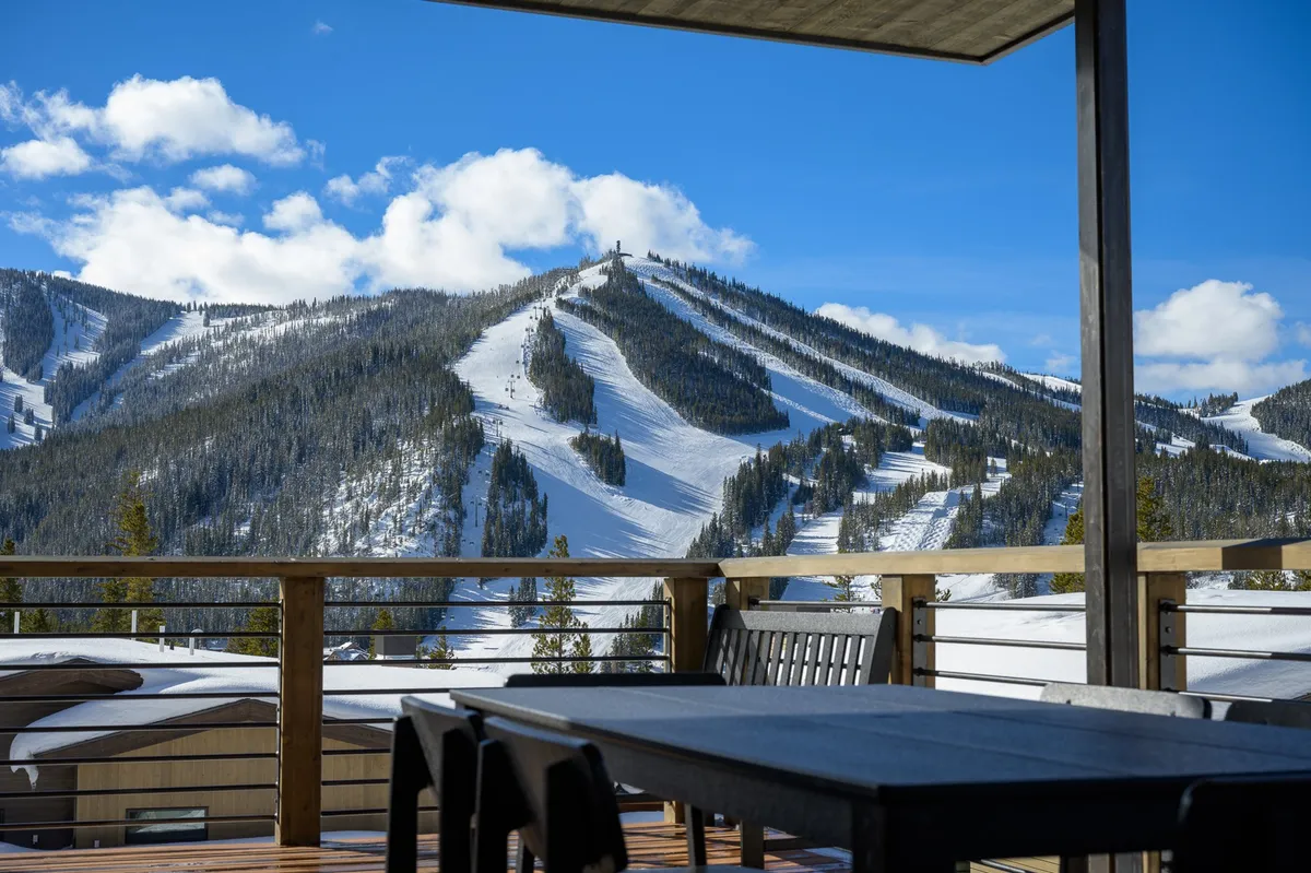 A serene outdoor seating area overlooking snow-covered mountain slopes under a clear blue sky. The space invites relaxation and offers sweeping views, perfectly capturing the alpine resort ambiance.